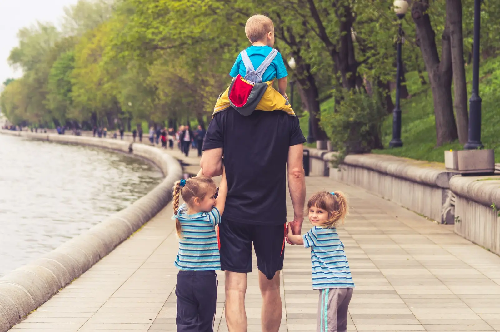 Vater mit drei Kindern auf einem Uferweg, ein Kind sitzt auf seinen Schultern