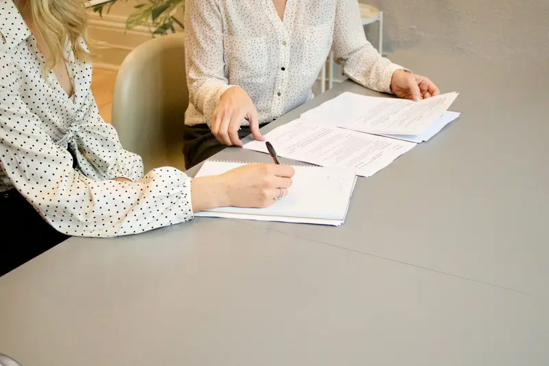 Zwei Frauen am Tisch, eine unterschreibt ein Dokument