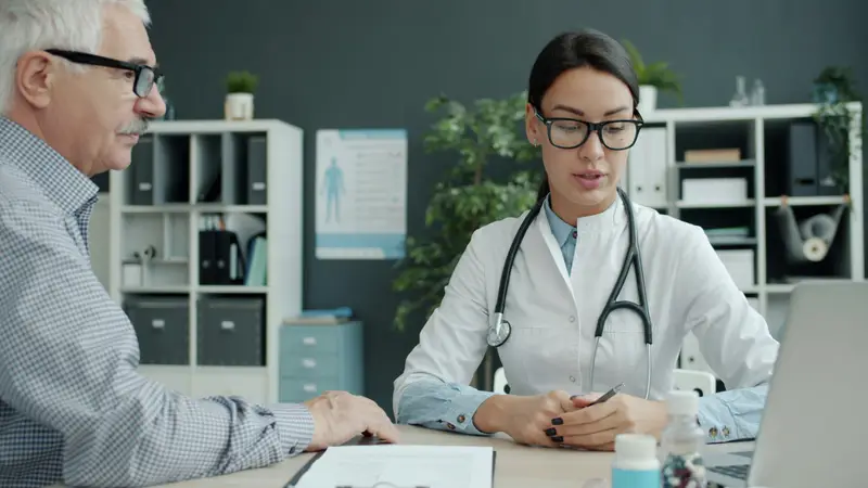 Ärztin im Gespräch mit einem älteren Patienten am Schreibtisch