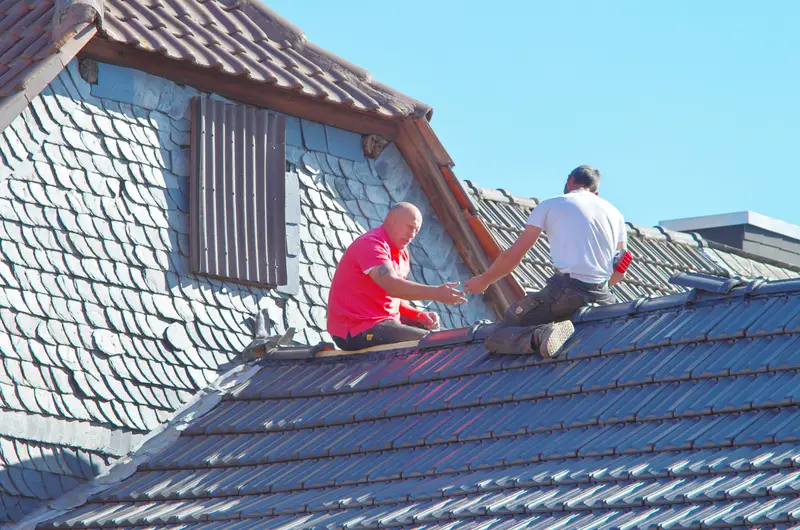 Zwei Dachdecker arbeiten an einem Dach mit Schiefergaube