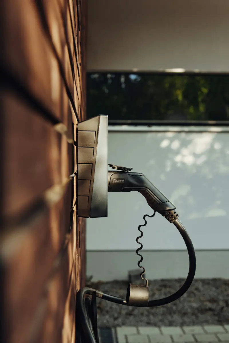Wallbox mit eingestecktem Ladekabel an einer dunklen Klinkerwand