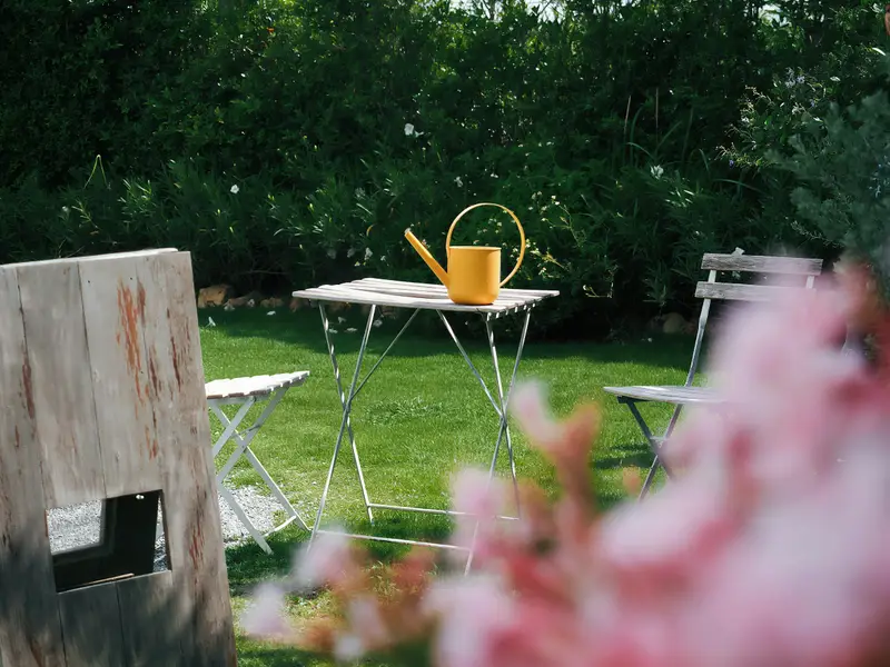 Kleiner Gartentisch mit gelber Gießkanne auf der Wiese