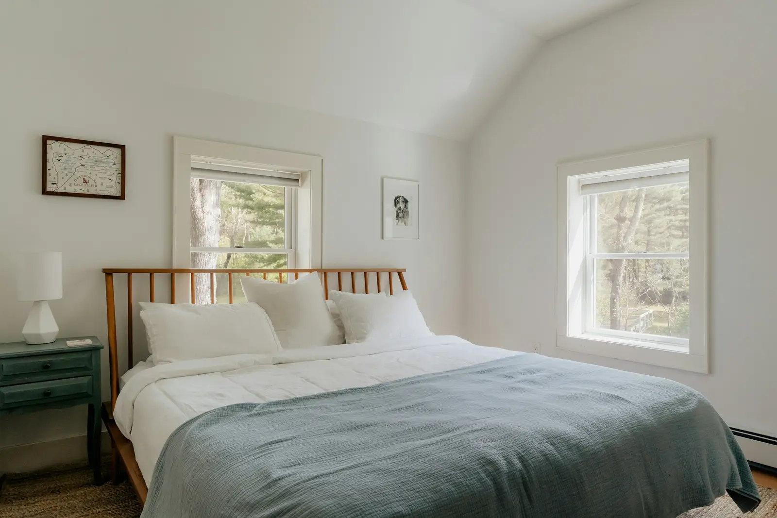 Helles Schlafzimmer mit Doppelbett, grauer Decke und zwei Fenstern