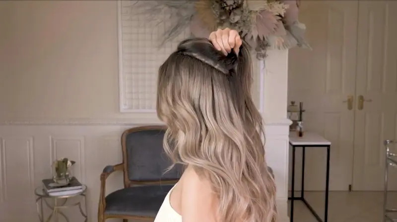 Frau mit langem, gewelltem Haar in hellen Balayage-Tönen, von hinten im Salon
