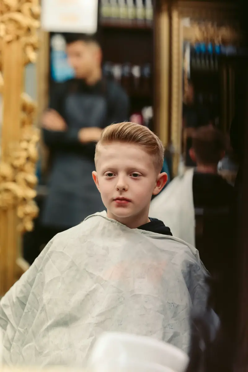 Junge im Friseurumhang beim Kinderhaarschnitt