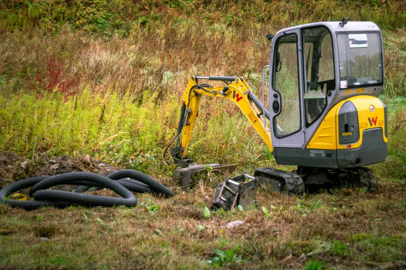 Minibagger auf einem Grundstück, daneben Drainagerohre