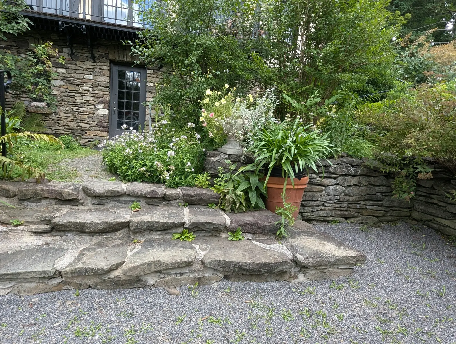 Treppe aus großen Natursteinplatten mit Trockenmauer und Stauden am Hang