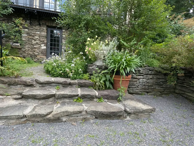 Treppe aus großen Natursteinplatten mit Trockenmauer und Stauden am Hang