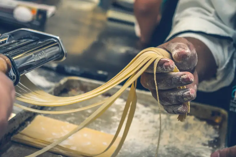 Hände ziehen frische Pasta aus der Nudelmaschine