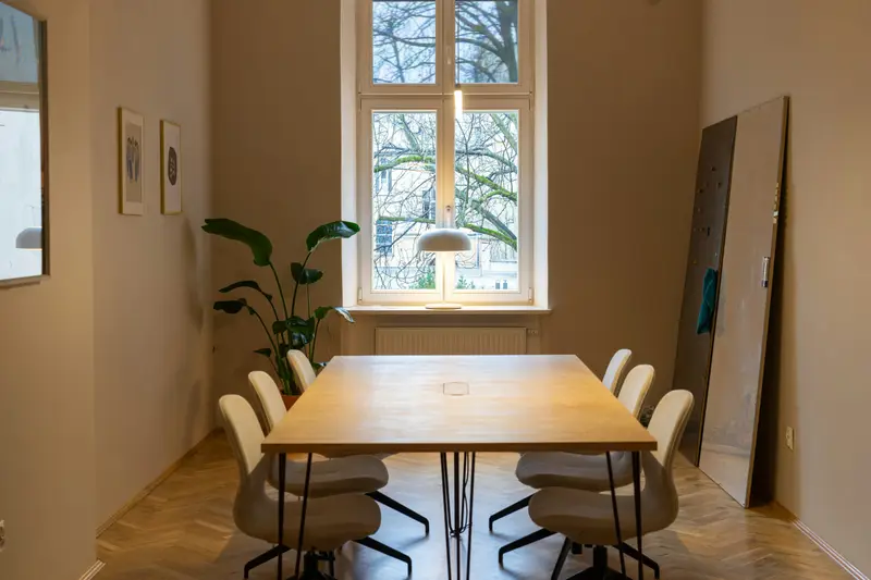 Besprechungsraum im Altbau mit hohem Sprossenfenster, Holztisch und Fischgrätparkett