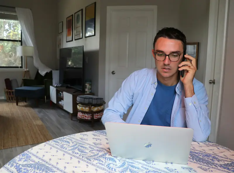 Mann telefoniert am Esstisch, vor sich den Laptop