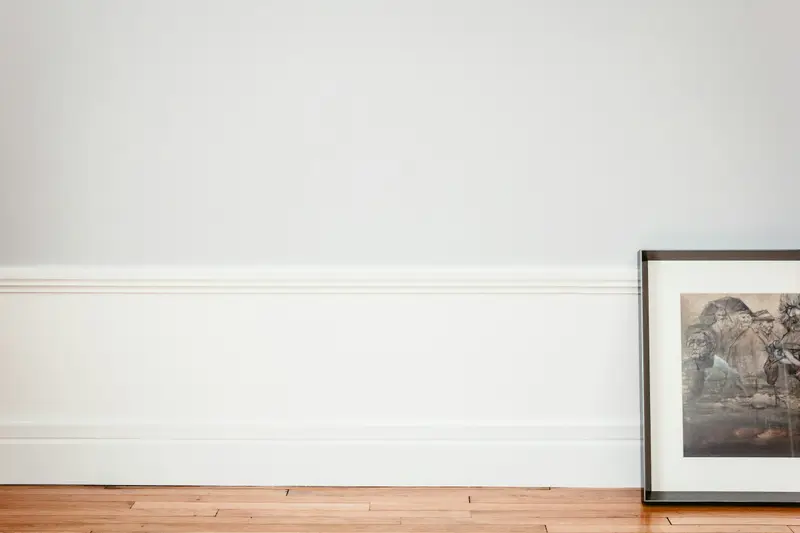 Leere Wand mit weißer Sockelleiste und angelehntem Bild auf Holzdielen
