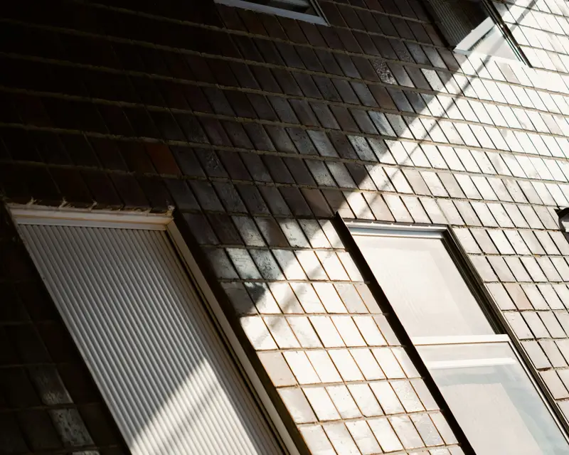 Zwei Dachfenster in einer Dachfläche aus dunklen Schindeln, Licht und Schatten