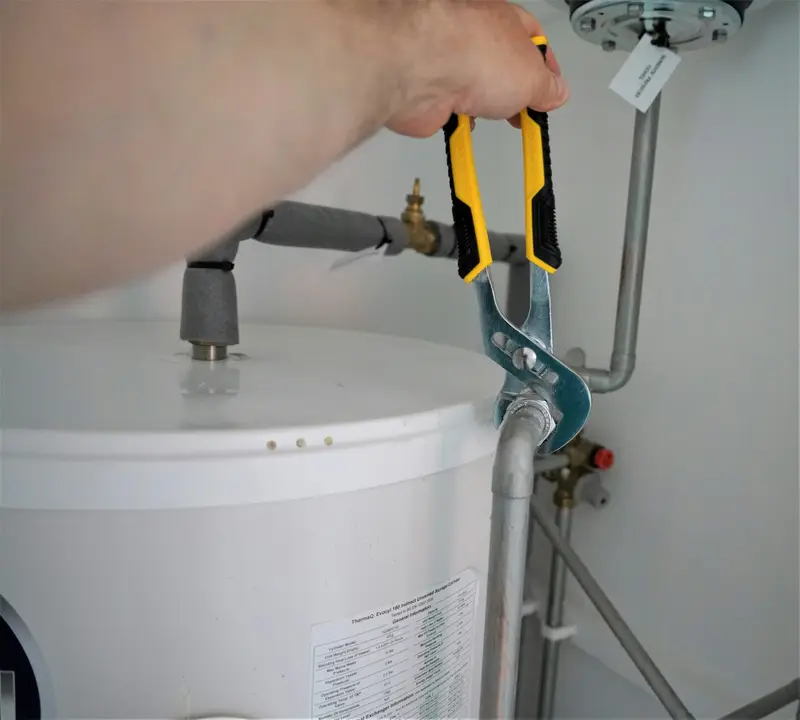 Installateur löst mit der Rohrzange einen Anschluss am Warmwasserspeicher