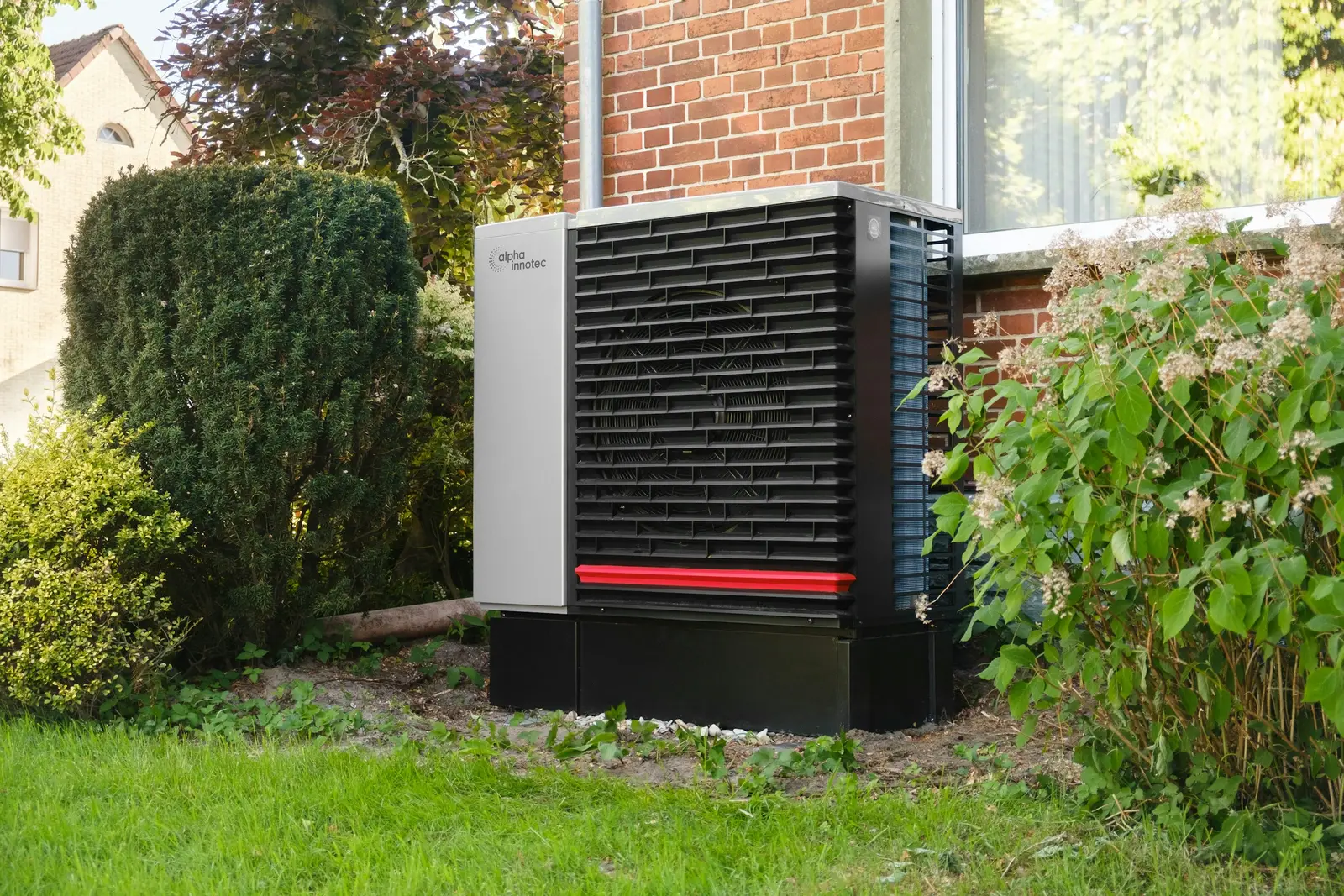 Wärmepumpe im Garten eines Einfamilienhauses mit Backsteinfassade