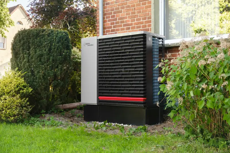 Wärmepumpe im Garten eines Einfamilienhauses mit Backsteinfassade